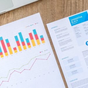 Top view of a laptop, charts, and resume on a wooden desk, showcasing business analysis and job application.